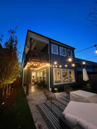 Backyard patio lit with bistro string lights and landscape uplighting at dusk in Charlotte, NC