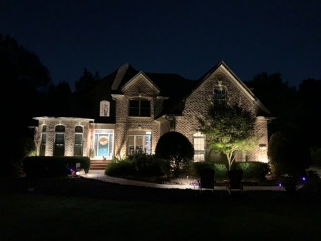 Landscape uplighting on a brick home's facade and front-yard tree with path lights in Charlotte, NC
